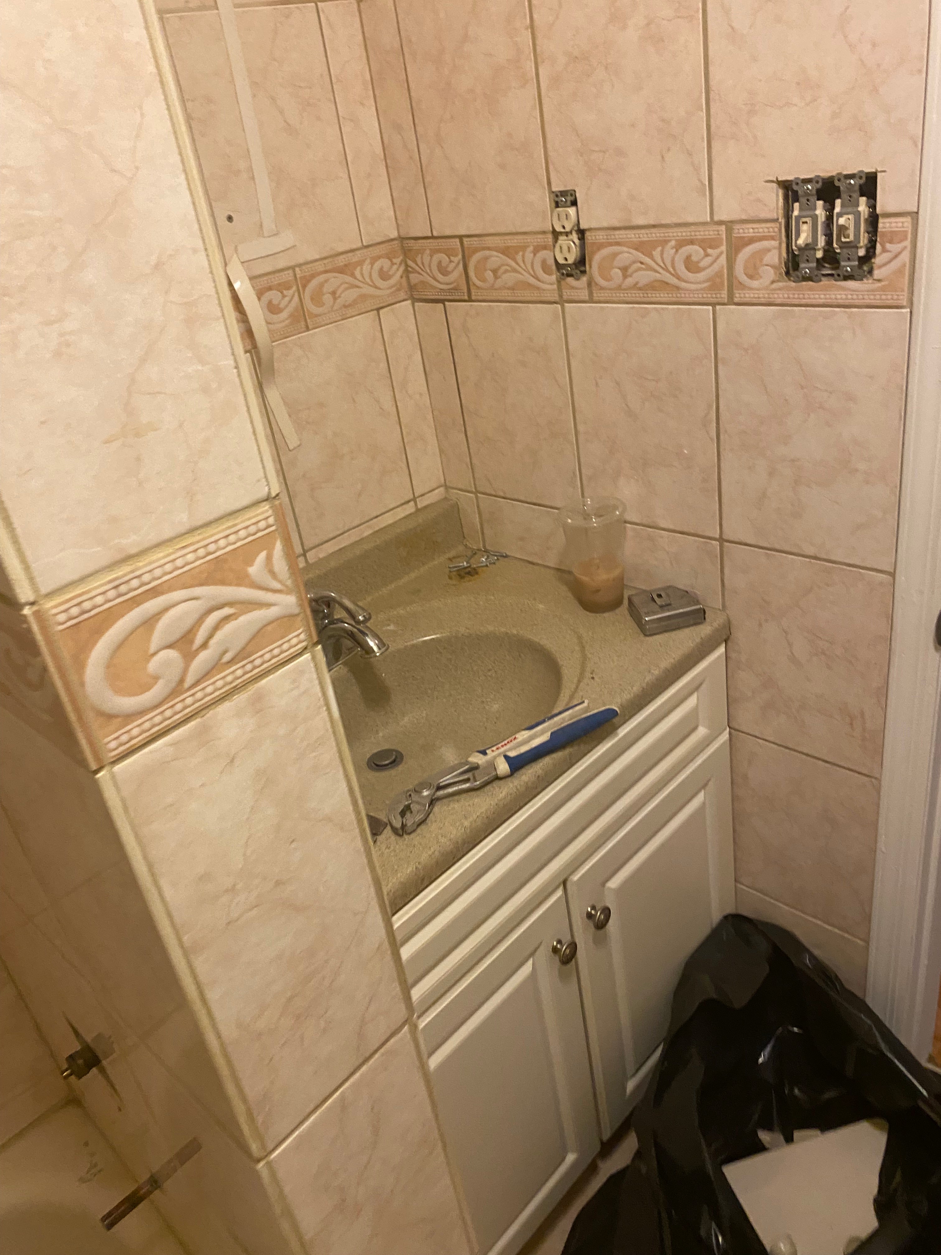 Bathroom corner with tiled walls, a mirror, and various tools on the counter.