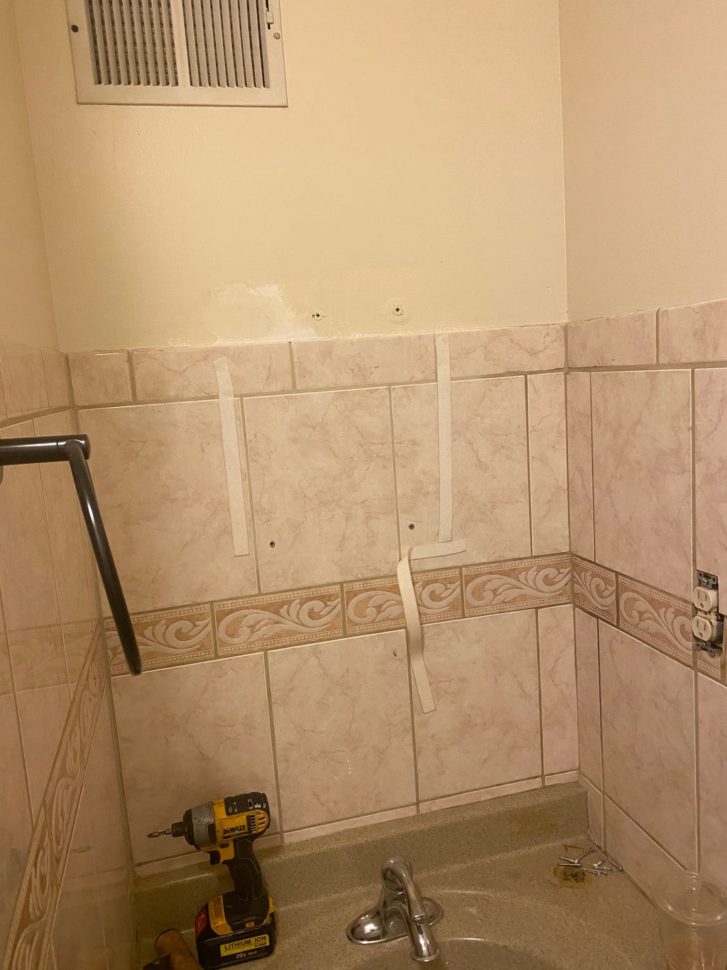 Bathroom corner with tiled walls, a drill, and a level.