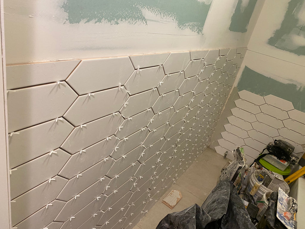 Hexagonal tiles being installed on a wall with tools and materials visible.