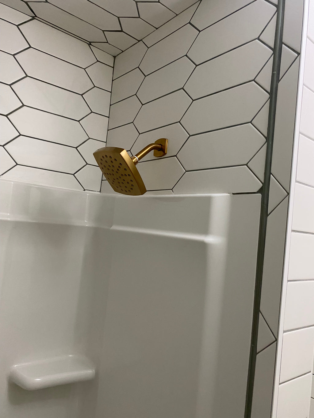 Gold shower head mounted on a tiled wall with a white bathtub.
