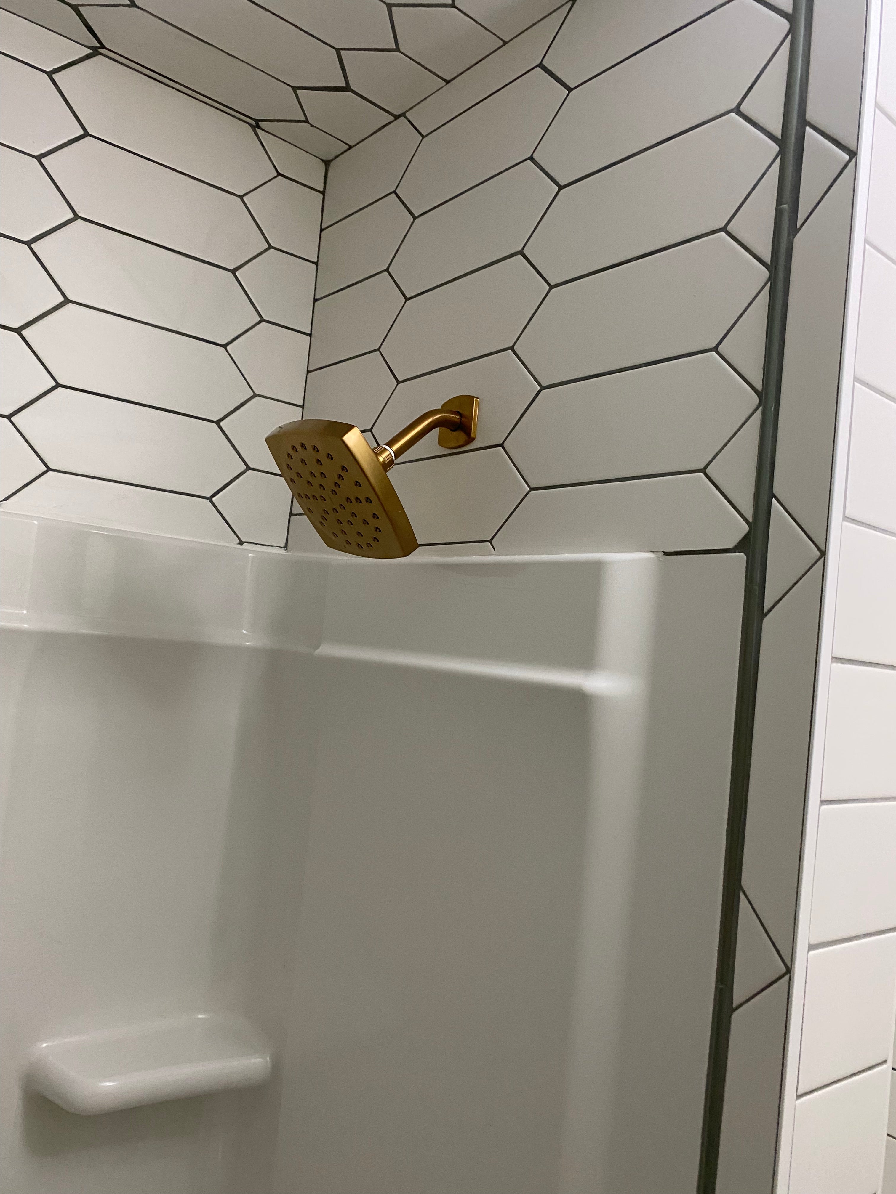 Gold shower head mounted on a tiled wall with a white bathtub.