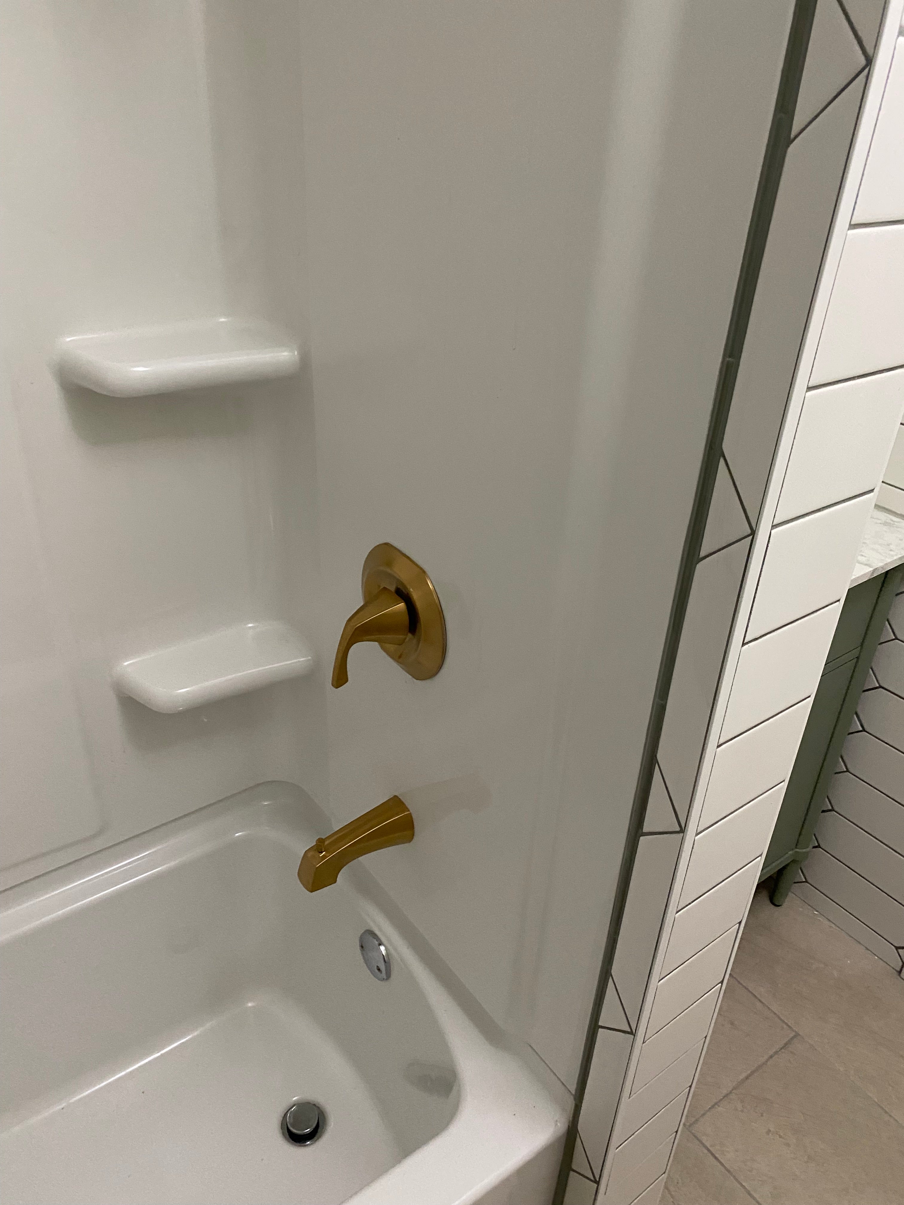 White bathtub with gold handles and tiled wall