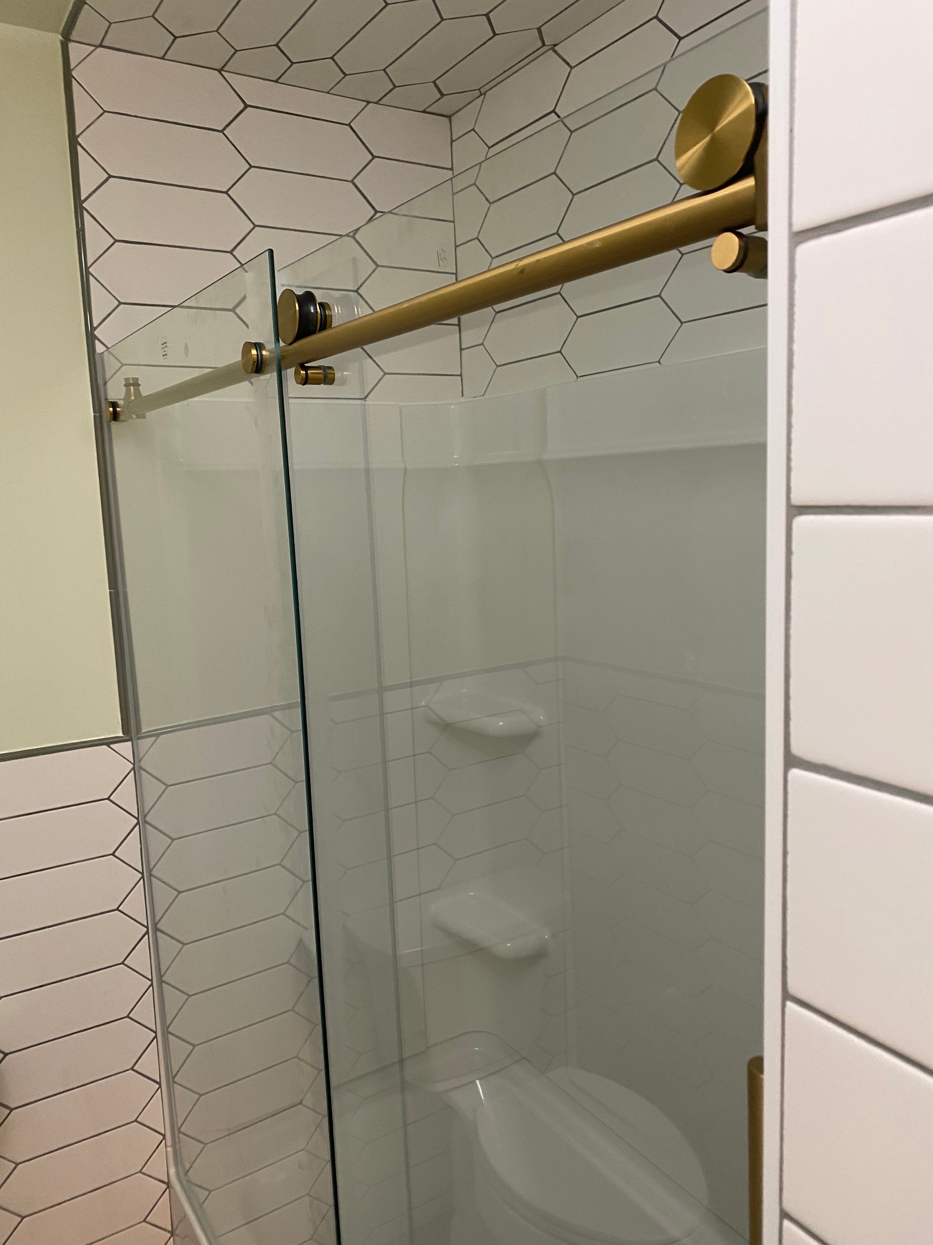 Finished bathroom renovation with glass shower enclosure with gold fixtures in a tiled bathroom