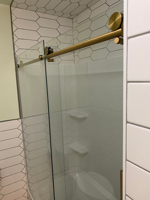 Finished bathroom renovation with glass shower enclosure with gold fixtures in a tiled bathroom